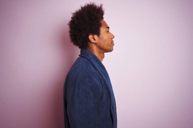 Genç afro-amerikan adam yan bakarak izole pembe arka plan üzerinde duran pijama giyen, kendine güvenen gülümseme ile doğal yüzü ile profil poz dinlenmek.