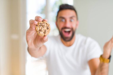 Yakışıklı İspanyol adam çikolata parçaları kurabiye yeme çok mutlu ve heyecanlı, kazanan ifade büyük bir gülümseme ile çığlık zafer kutluyor ve ellerini kaldırdı