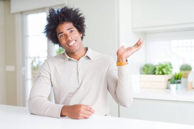 Afrika kökenli Amerikalı adam evde neşeli sunulması ve kameraya bakarak avucunun ile işaret gülümseyen.
