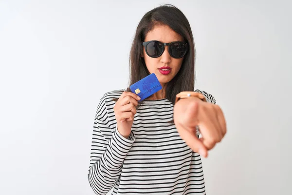 Young chinese woman wearing sunglasses holding credit card over isolated white background pointing with finger to the camera and to you, hand sign, positive and confident gesture from the front