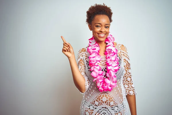 Young african american woman with afro hair wearing flower hawaiian lei over isolated background with a big smile on face, pointing with hand and finger to the side looking at the camera.