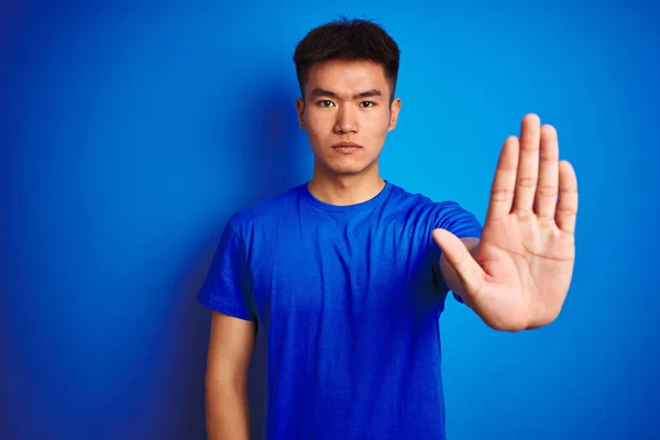 年轻的亚洲中国男子穿着T恤站在孤立的蓝色背景做停止唱歌与手掌 警告表情 脸上带有负面和严肃的手势 — 图库照片