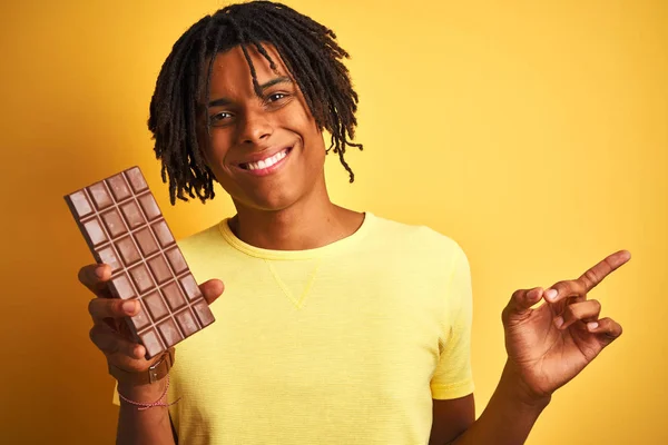 Afro Americký Muž Dredy Pojídáním Čokoládového Baru Přes Izolované Žluté — Stock fotografie