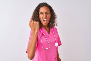 Genç Brezilyalı hemşire kadın izole beyaz arka plan üzerinde duran stetoskop giyen kızgın ve öfkeli yükselterek yumruk sinirli ve öfkeli öfke ile bağırırken. Öfke ve agresif kavram.