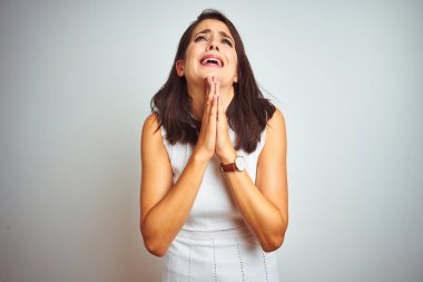 Beyaz izole arka plan üzerinde duran elbise giyen genç güzel kadın dilencilik ve umut ifadesi ile birlikte elleri ile dua çok duygusal ve endişeli yüzünde. Af dilemek istiyorum. Din kavramı.