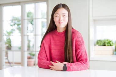 Güzel Asyalı kadın komik yüzü ile yanakları şişirme beyaz masada pembe kazak giyiyor. Ağız hava ile şişirilmiş, deli ifade.