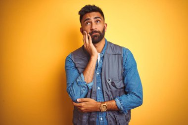 Yakışıklı hint teknisyen adam izole sarı arka plan üzerinde üniforma giyen yorgun görünümlü ve çapraz kolları ile depresyon sorunları ile sıkılmış düşünme.