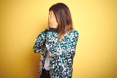 Genç güzel kadın sarı izole arka plan üzerinde rahat ceket giyen üzgün ifade ile elleri ile yüz kapsayan ağlarken. Depresyon kavramı.