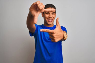 Genç yakışıklı Arap adam mavi t-shirt izole beyaz arka plan üzerinde duran giyen mutlu yüz ile elleri ve parmakları ile çerçeve yapma gülümseyerek. Yaratıcılık ve fotoğrafçılık konsepti.