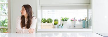 Güzel genç kadın evde beyaz masaya oturan geniş açı resim emin gülümseme ile doğal yüz pozuyla profil rahatla tarafına, seyir.