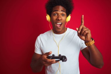 Afro oyun adam izole kırmızı arka plan üzerinde joystick kulaklık kullanarak video oyunu oynarken mutlu yüz, bir numara ile bir fikir veya soru işaret parmağı ile şaşırttı