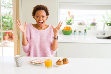 Genç afro-amerikan kadın evde sabah breaksfast yeme deli kutluyor ve kollarını kaldırdı ve açık gözleri heyecan çığlık ile başarı için hayran. Kazanan kavramı