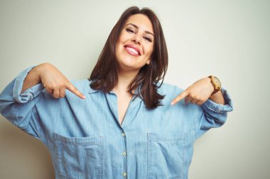 Genç güzel esmer kadın izole arka plan üzerinde rahat mavi kot gömlek giyen yüzünde gülümseme ile emin görünümlü, parmakları gururlu ve mutlu kendini işaret.