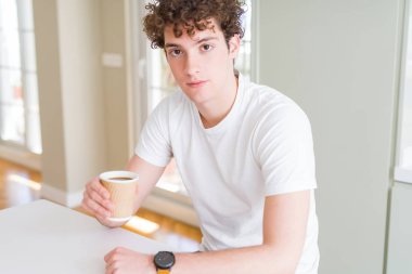 İçen genç adam evde bir fincan kahve yiyerek akıllı yüzünde ki kendine güvenen ifadeyle ciddi düşünüyor