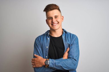 Denim gömlek giyen genç yakışıklı adam izole beyaz arka plan üzerinde duran mutlu yüz kameraya bakarak çapraz kolları ile gülümseyerek. Pozitif kişi.