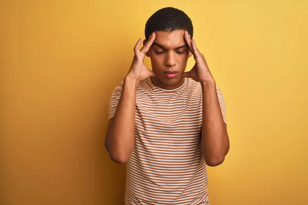 年轻的英俊阿拉伯男子穿着条纹T恤站在孤立的黄色背景上 手放在头上 因为压力而感到头部疼痛 患有偏头痛 — 图库照片