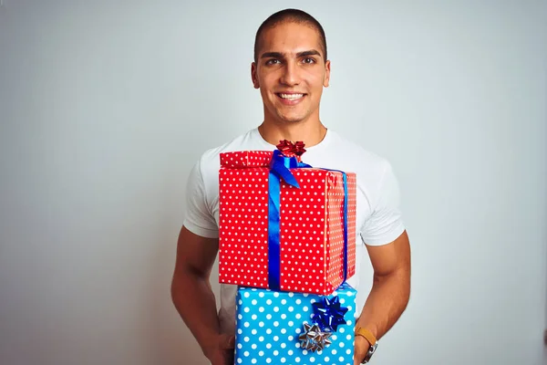 Young handsome man holding birthday gifts over white isolated background with a happy face standing and smiling with a confident smile showing teeth