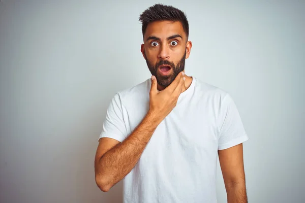 Young indian man wearing t-shirt standing over isolated white background Looking fascinated with disbelief, surprise and amazed expression with hands on chin