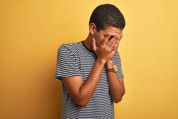 年轻的英俊阿拉伯男子穿着海军条纹T恤在孤立的黄色背景与悲伤的表情覆盖脸与双手 而哭泣 抑郁症概念 — 图库照片