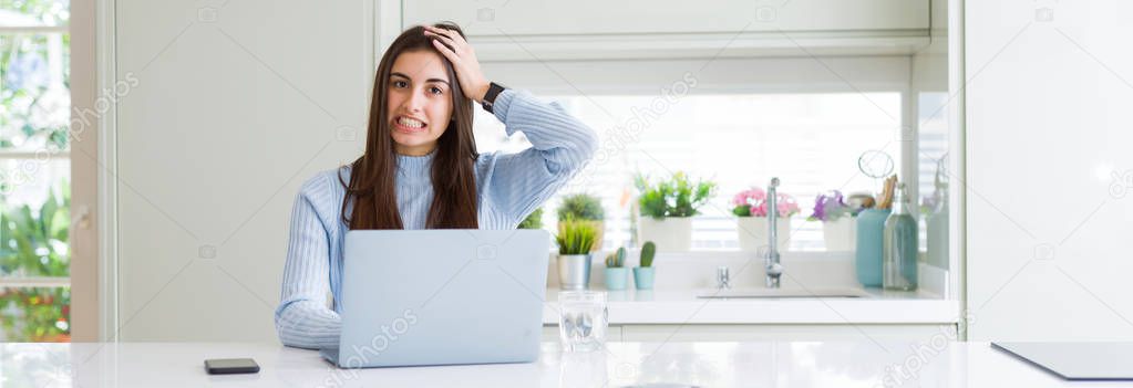 Wide angle picture of beautiful young woman working or studying using laptop stressed with hand on head, shocked with shame and surprise face, angry and frustrated. Fear and upset for mistake.