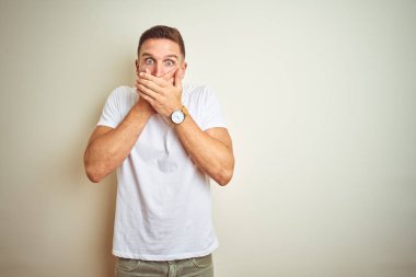 Üzerinde rahat beyaz t-shirt giyen genç yakışıklı adam arka plan ağız hata için elleriyle kapsayan şok izole. Gizli kavramı.