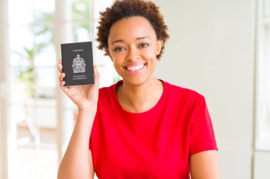 Genç afro-amerikan kadın ayakta mutlu bir yüz ile Kanada pasaportu tutan ve dişleri gösteren kendinden emin bir gülümseme ile gülümseyerek