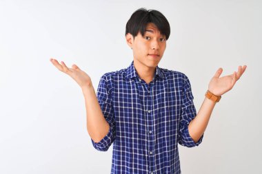 Izole beyaz arka plan üzerinde duran rahat mavi gömlek giyen genç Çinli adam silah ve elleri kaldırdı ile anlamsız ve karışık ifade. Şüphe kavramı.