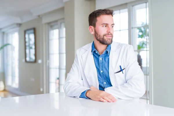 英俊的医生男子穿着医疗外套在诊所看着远方 面带微笑 自然表情 笑自信 — 图库照片