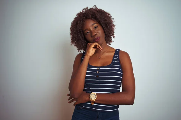 Young african afro woman wearing striped t-shirt standing over isolated white background with hand on chin thinking about question, pensive expression. Smiling with thoughtful face. Doubt concept.