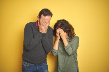 Ağlarken elleri ile yüz kapsayan üzgün ifade ile izole sarı arka plan üzerinde güzel orta yaş çift. Depresyon kavramı.