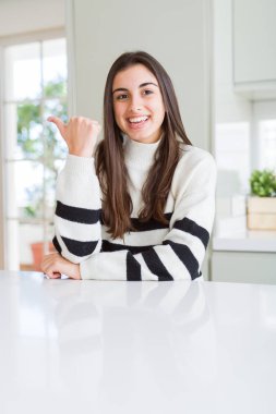 Seyir ve başparmak yanında yukarıyı mutlu yüz ile gülümseyen çizgili Süveter giyen güzel genç kadın.