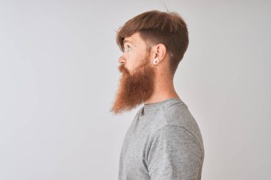 Genç kızıl saçlı İrlandalı adam yan bakarak izole gri arka plan üzerinde duran t-shirt giyen, kendine güvenen gülümseme ile doğal yüzü ile profil poz dinlenmek.