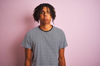 Komik yüzü ile izole pembe arka plan şişirme yanakları üzerinde duran lacivert çizgili t-shirt giyen dreadlocks ile Afro adam. Ağız hava ile şişirilmiş, deli ifade.