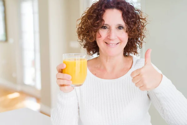 资深女人抚摸着一杯新鲜的橙汁高兴 大笑着做Ok标志 用手指竖起大拇指 优秀标志 — 图库照片