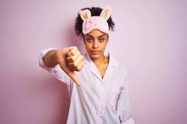 年轻的非洲裔美国妇女穿着睡衣和面具在孤立的粉红色背景看起来不高兴和愤怒显示拒绝和消极与拇指向下手势 表达错误 — 图库照片