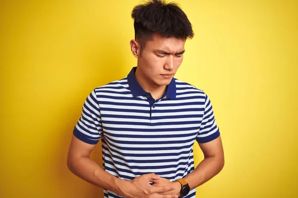 若いアジアの中国人男性は 吐き気 痛みを伴う病気の気分が悪いので 胃の上に孤立した黄色の背景の上に立ってストライプポロを身に着けている 痛い概念 — ストック写真