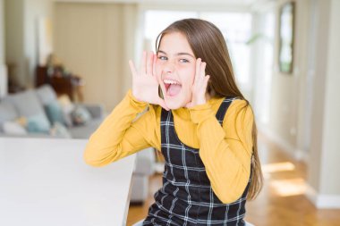 Güzel genç kız çocuk masada bağırarak oturan ve ağız da el ile yan yüksek sesle bağırıyor. İletişim kavramı.