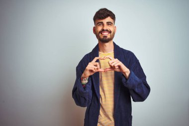 Dövme giyen genç adam izole beyaz arka plan üzerinde duran sevgi kalp sembolü ve elleriyle şekil gösteren gülümseyerek bornoz giyen. Romantik kavram.