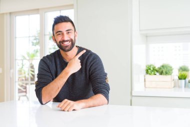 Yakışıklı İspanyol adam evde neşeli rahat kazak giyen yüzünde mutlu ve doğal ifade ile yan yana el ve parmak ile işaret yüz bir gülümseme ile neşeli