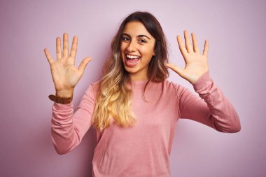 Genç güzel kadın pembe izole arka plan üzerinde bir kazak giyen gösteren ve emin ve mutlu gülümserken parmakları on numara ile işaret.