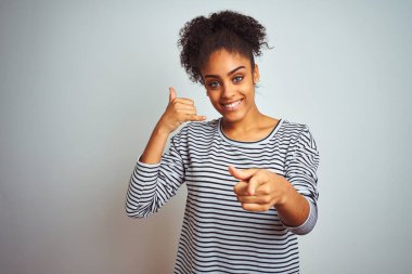 Lacivert çizgili tişört giyen Afro-amerikan kadın izole beyaz arka plan üzerinde durarak gülümseyerek telefon jesti konuşan ve sizi işaret ediyor. Beni ara.