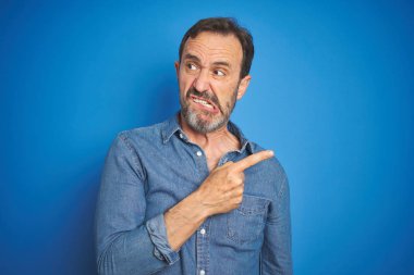Izole mavi arka plan üzerinde gri saçlı yakışıklı orta yaş yaşlı adam kenara işaret parmağı ile endişeli ve sinir işaret, endişeli ve sürpriz ifade