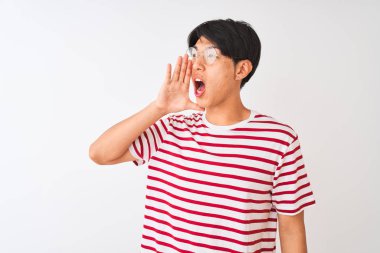 Genç Çinli adam gözlük ve çizgili t-shirt izole beyaz arka plan üzerinde bağırarak ve ağız da el ile yan yüksek sesle çığlık ayakta giyiyor. İletişim kavramı.