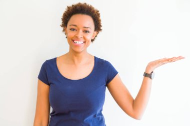Beyaz arka plan üzerinde genç güzel afro-amerikan kadın gülümseyen neşeli sunan ve avuç içi ile işaret kameraya bakarak.