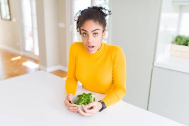 Genç afro-amerikan kız heatlhy yeşil brokoli yeme sürpriz bir yüz ile şok korkmuş, korku ifade korku ve heyecanlı