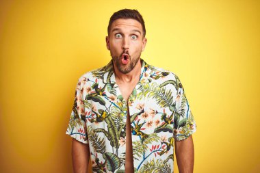 Yakışıklı adam sarı izole arka plan üzerinde yaz hawaii çiçek gömlek giyen korkmuş ve sürpriz ifade, korku ve heyecanlı yüz ile şok.