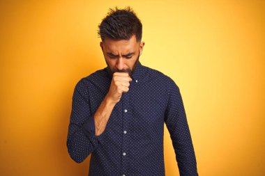 Genç yakışıklı hintli işadamı izole sarı arka plan üzerinde gömlek giyen rahatsız hissediyorum ve soğuk veya bronşit için bir belirti olarak öksürük. Sağlık kavramı.