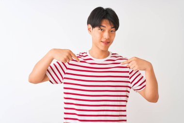 Izole beyaz arka plan üzerinde duran rahat çizgili t-shirt giyen genç Çinli adam yüzünde gülümseme ile emin görünümlü, parmakları gururlu ve mutlu kendini işaret.