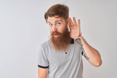 Genç kızıl İrlandalı adam izole beyaz arka plan üzerinde duran gri polo giyen el kulak üzerinden söylenti veya dedikodu bir işitme dinlerken gülümseyerek. Sağırlık kavramı.
