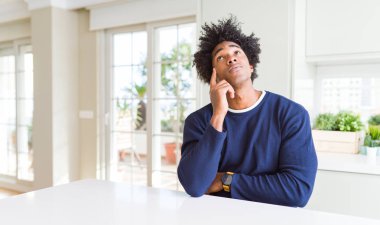 Genç afro-amerikan adam gündelik kazak giyen çenesi üzerinde el ile evde oturan soru, dalgın ifade düşünme. Düşünceli bir yüzle gülümsüyor. Şüphe kavramı.